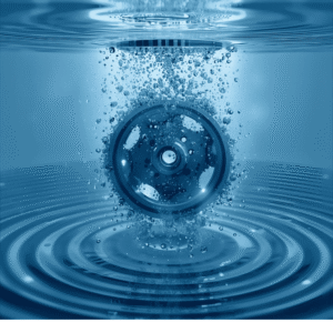 Esta imagen muestra un engranaje metálico sumergido en agua azul con burbujas visibles